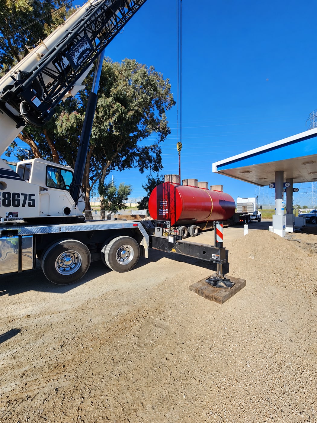 Crane and truck handling a fuel tank at a gas station construction site